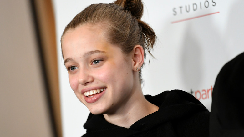 Shiloh Jolie-Pitt smiles in a black hoodie. 