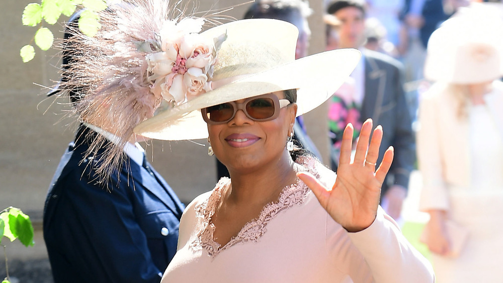 Oprah Winfrey in a feathery large hat and sunglasses waving 