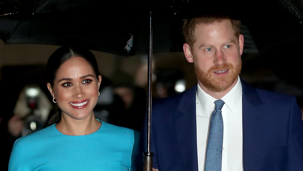 Meghan Markle and Prince Harry smiling under an umbrella