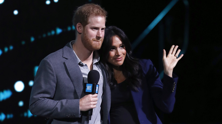 Prince Harry and Meghan Markle smiling while on stage at an event