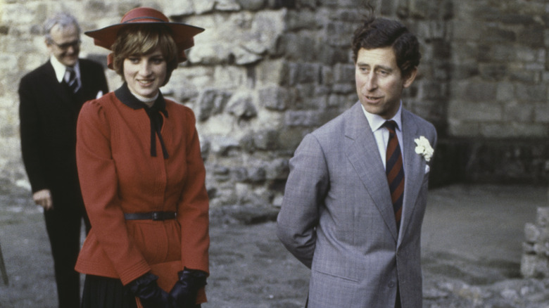 Princess Diana wears a red dress while King Charles III looks on