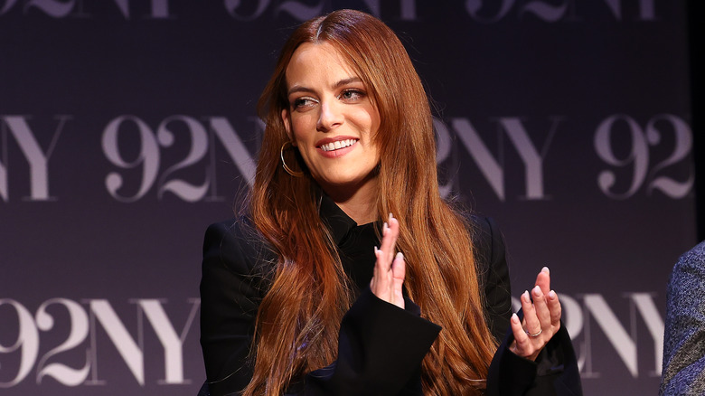 Riley Keough with long red hair, clapping