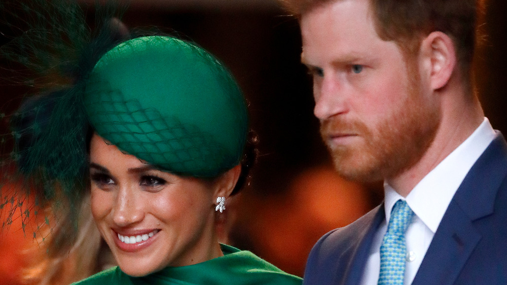 Meghan Markle in green hat with frowning Prince Harry