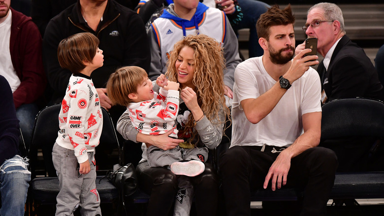 Shakira holding children while Gerard Piqué holds phone