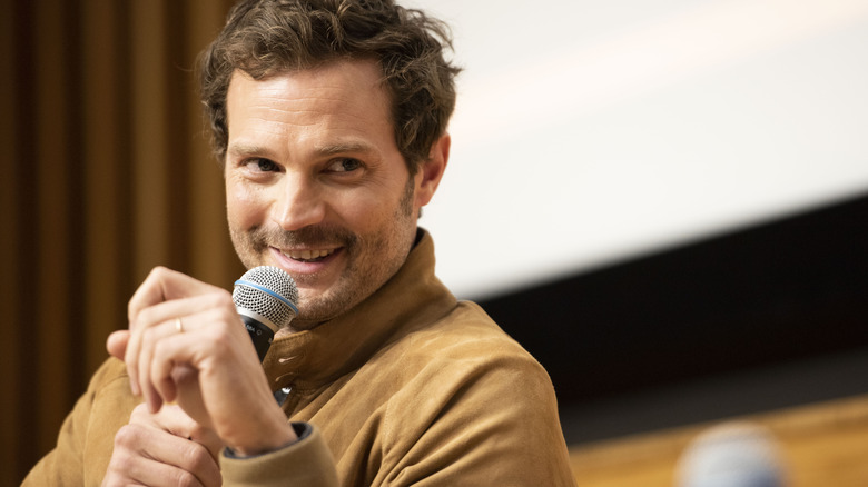 Jamie Dornan smiling and speaking into microphone