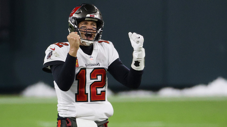 Tom Brady yelling on football field, arms raised in fists