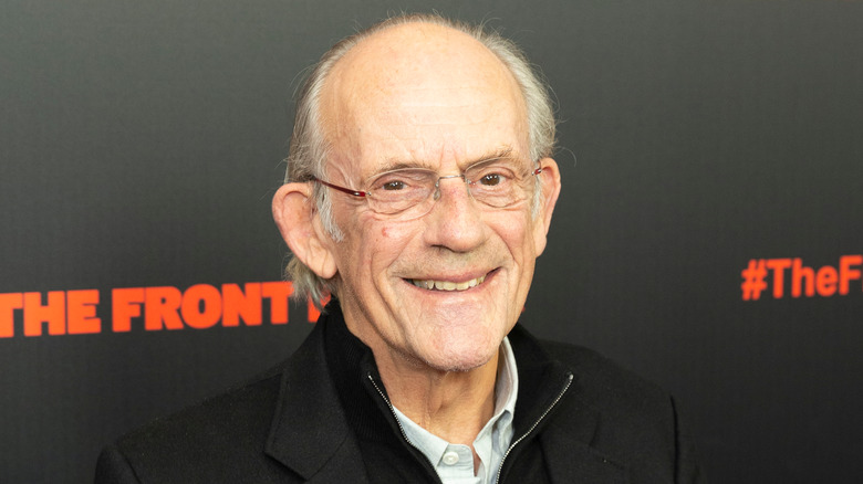 Christopher Lloyd smiles while wearing a black jacket and blue top