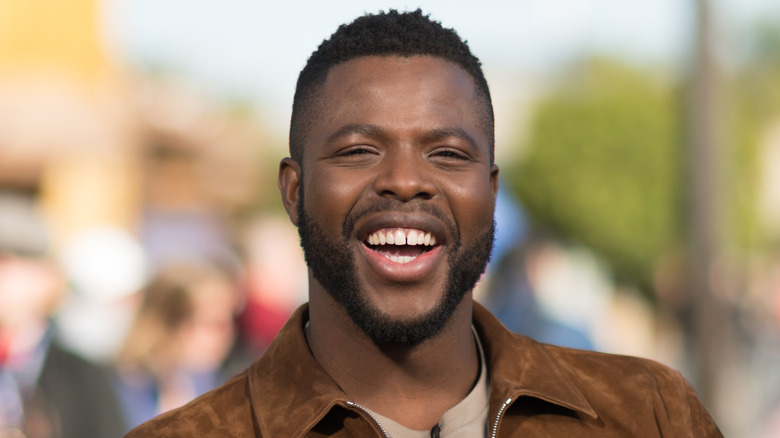 Winston Duke laughing, brown jacket