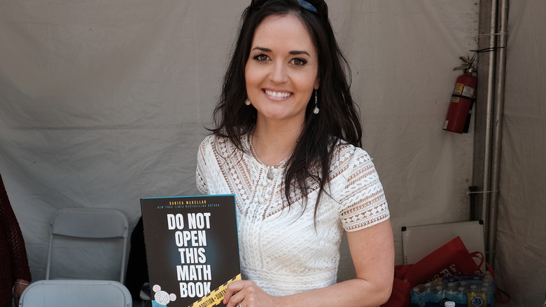 Danica McKellar smiling while holding her book, "Do Not Open This Math Book"