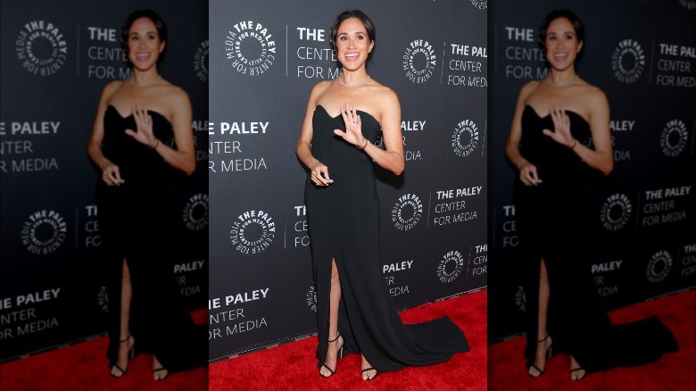 Meghan Markle wearing a black dress and waving on the Paley Honor red carpet